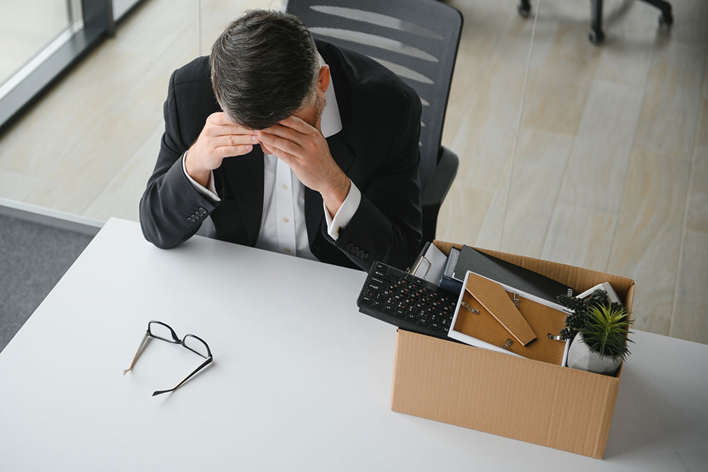 Older employee leaving the office with a box of personal belongings after job loss